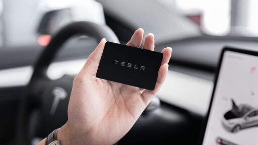 Tesla Insurance, Close-up of a hand holding a key card inside a modern car interior with digital display.